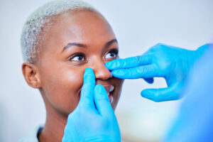 Doctor's hands wearing blue gloves, touching a woman's nose for Endoscopic sinus surgery