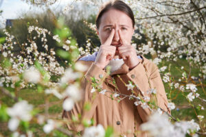 Woman suffering from seasonal allergy at springtime with flowers all around her.