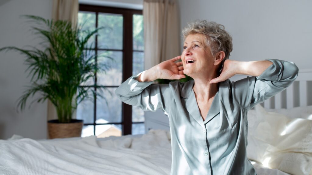 Cheerful senior woman in bed at home getting up.