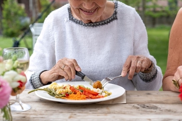Elderly woman outdoors eating a good meal.
