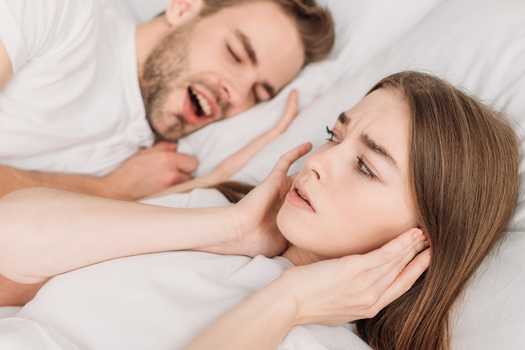 Man snoring and woman plugging ears with hands.
