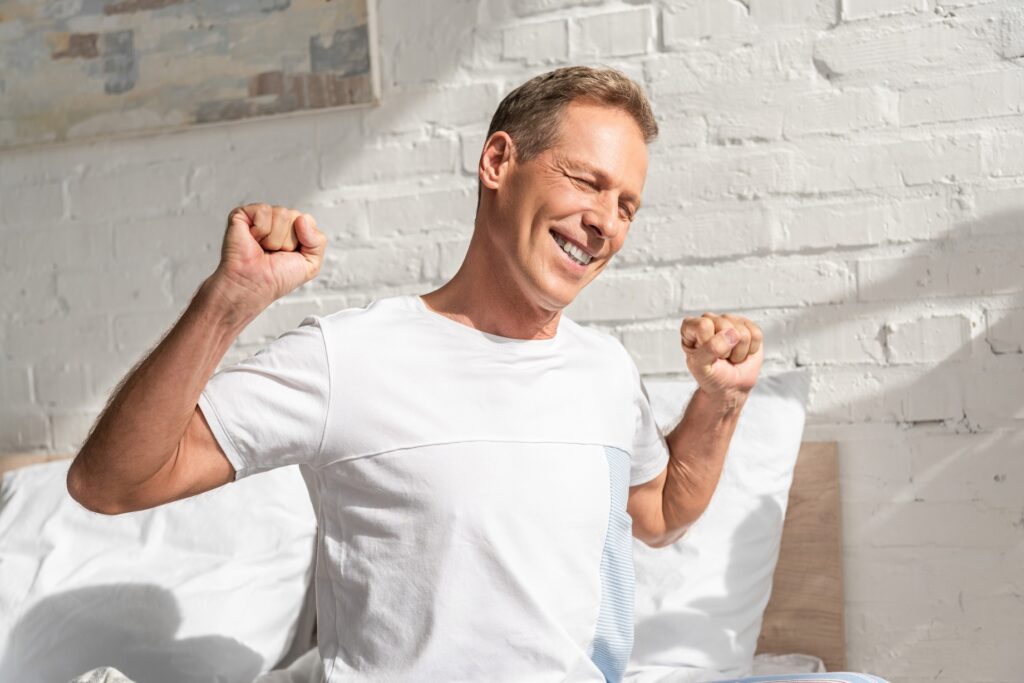 Smiling man stretching while sitting on bed after great night sleep from Inspire Implant.