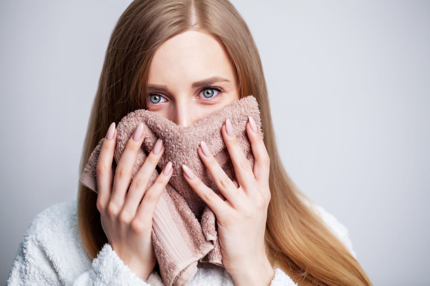 Woman holds a warm damp cloth to her face.